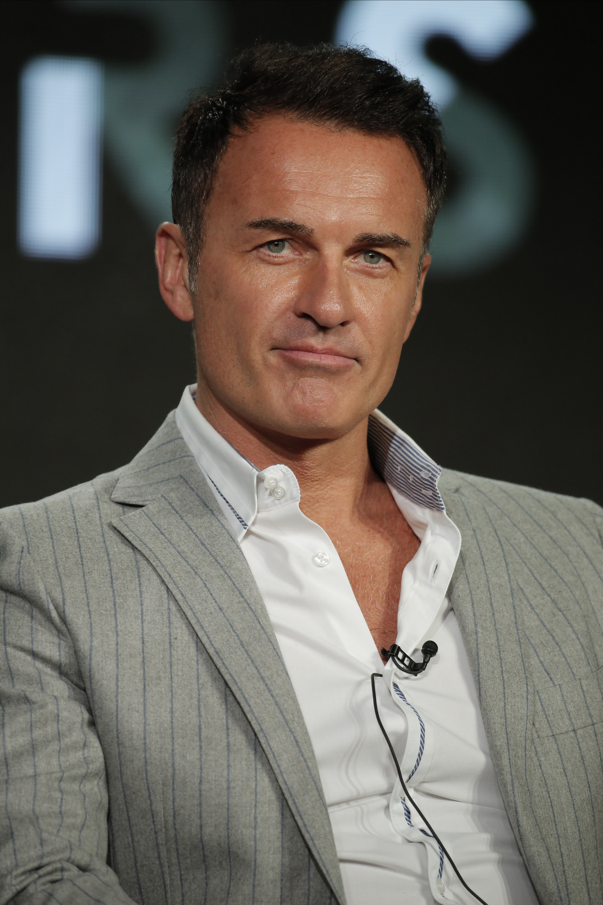 Man in a pinstripe suit with a microphone, against a blurred background.