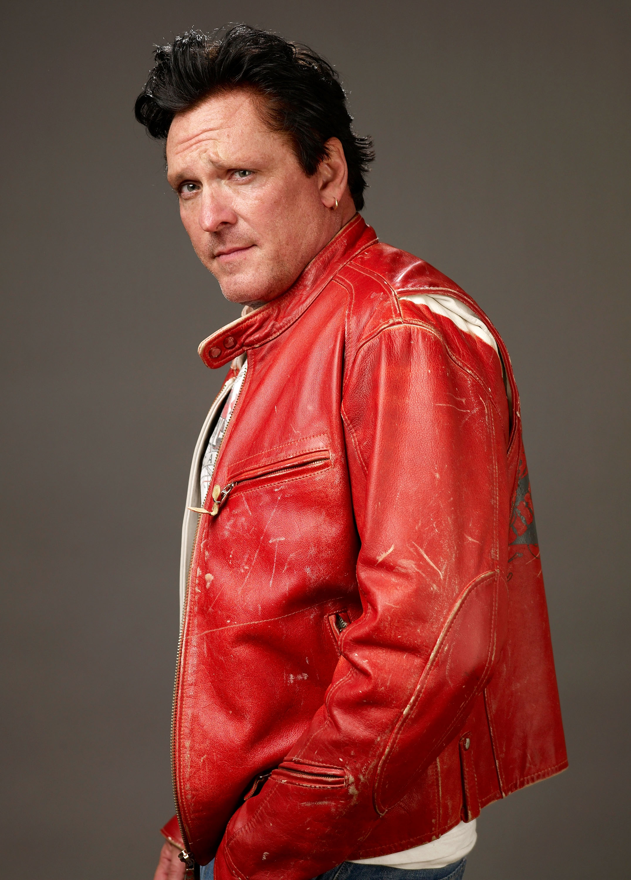 Man in a red leather jacket looking to the side against a gray background.
