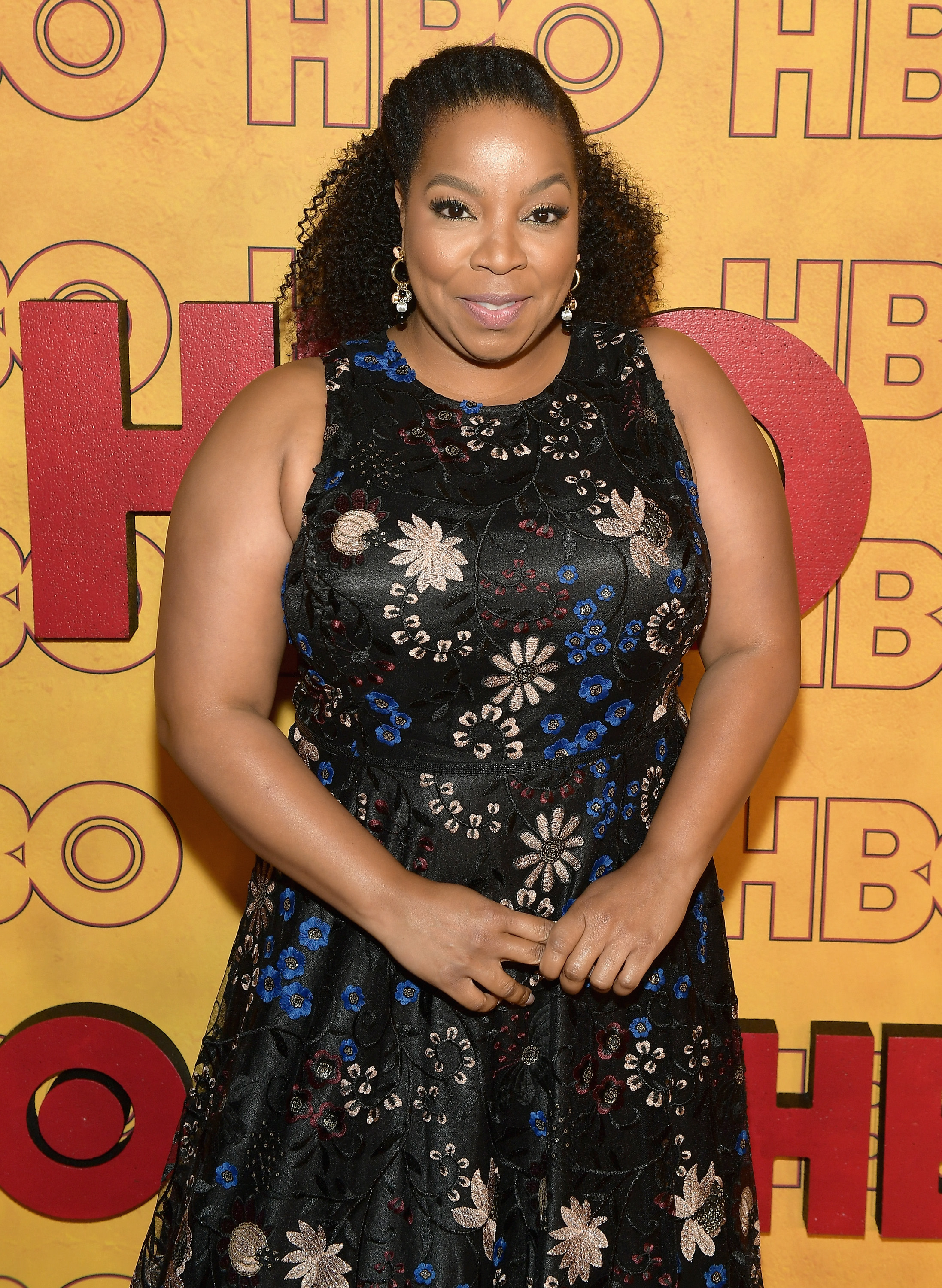 A woman in a floral dress poses in front of an HBO backdrop.