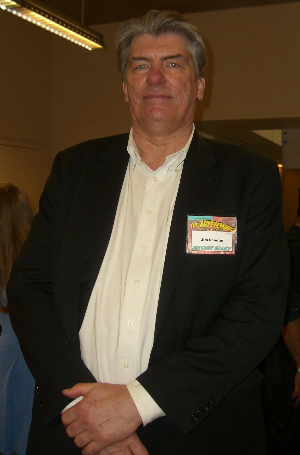 A man in a black suit and white shirt with a name tag that reads
