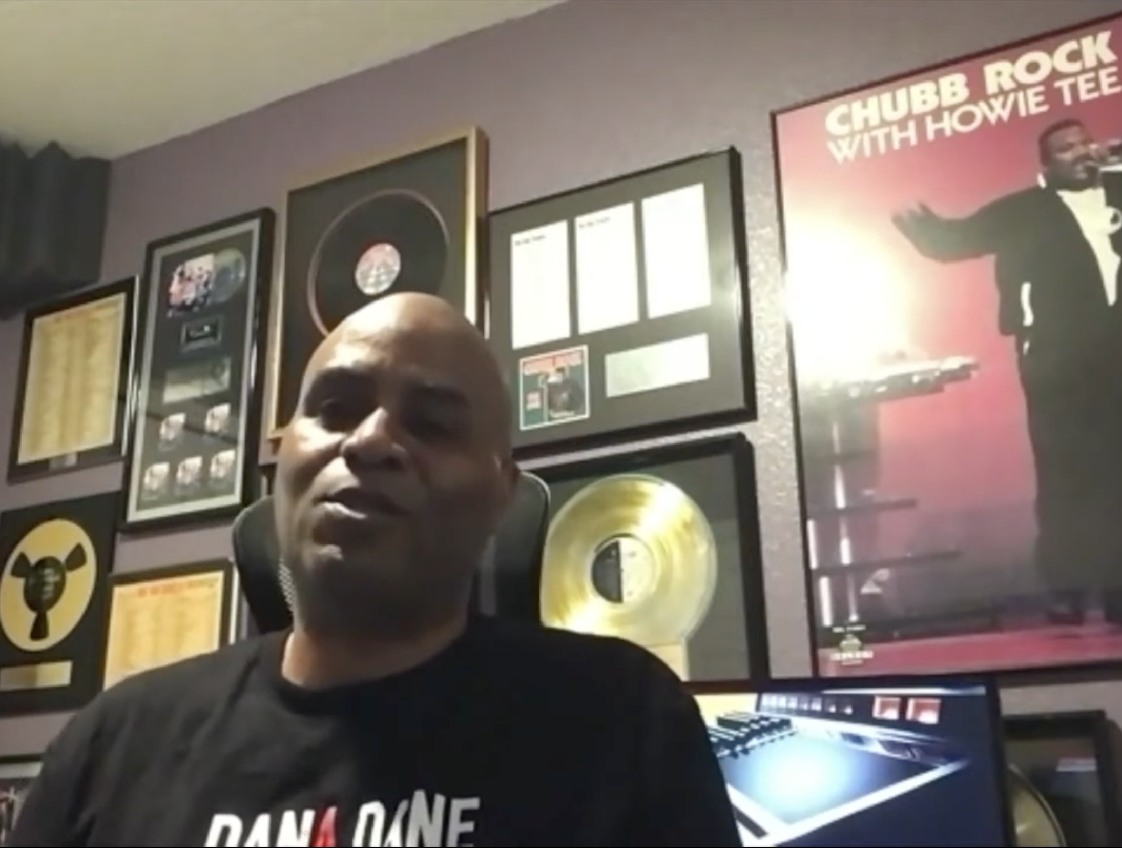A man sits in a room with music awards on the wall, including a Chubb Rock poster.