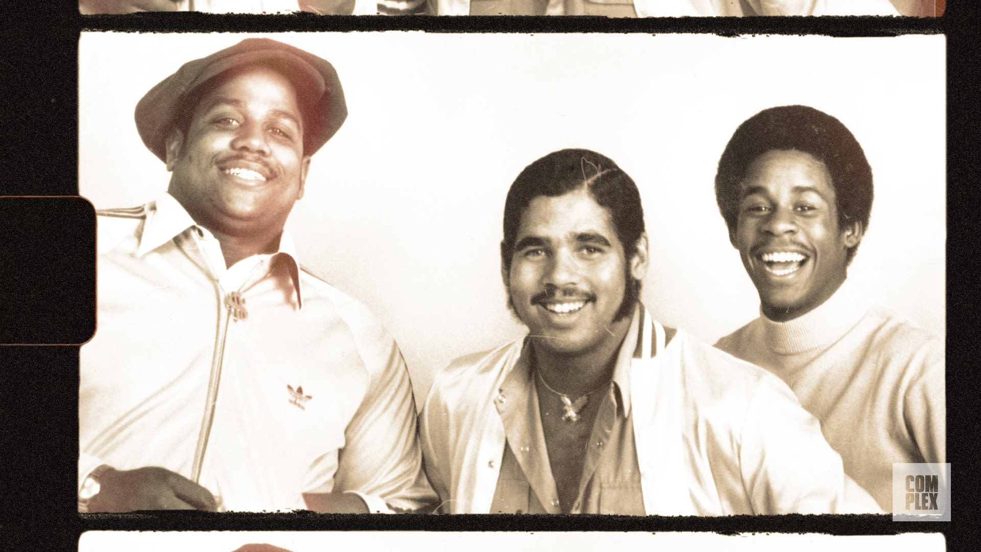 Three men smiling in a vintage photo. One wears a cap, another has a mustache, and the third has an afro.
