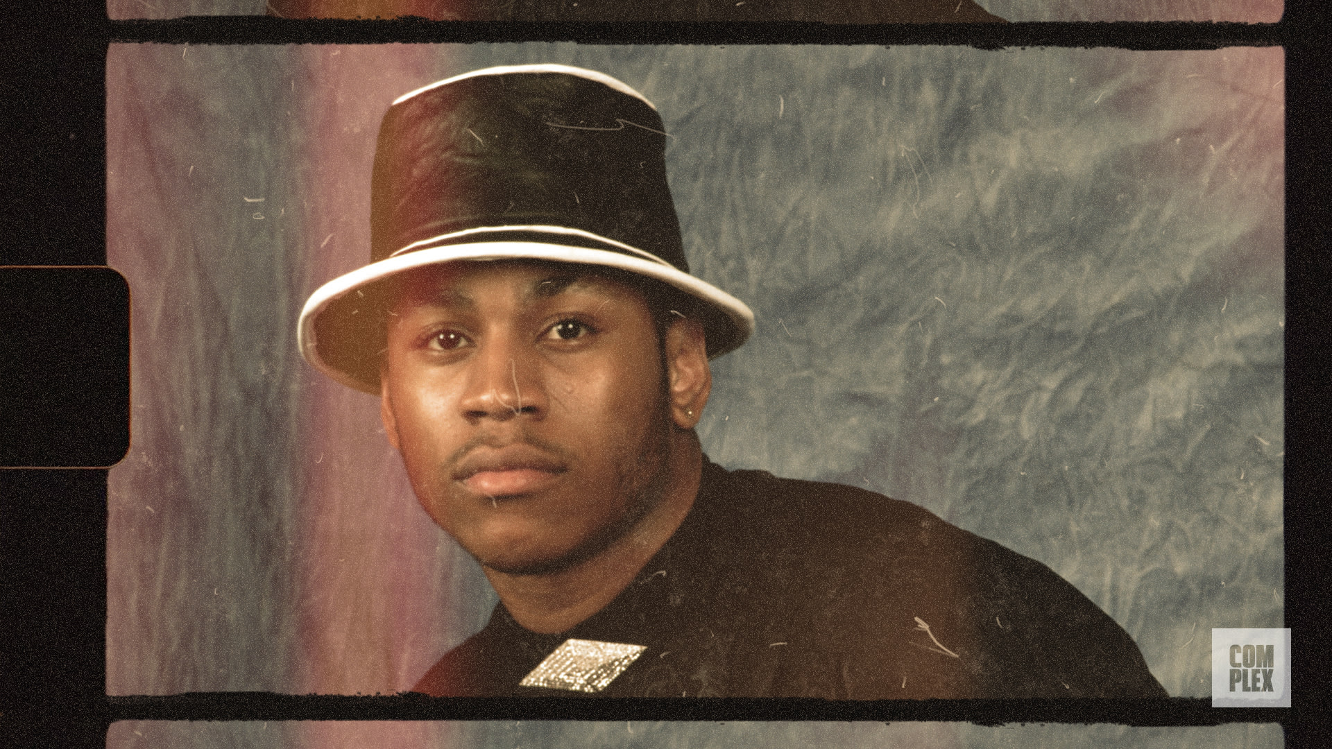 A person wearing a black bucket hat and a black shirt with a reflective patch, set against a textured blue backdrop.