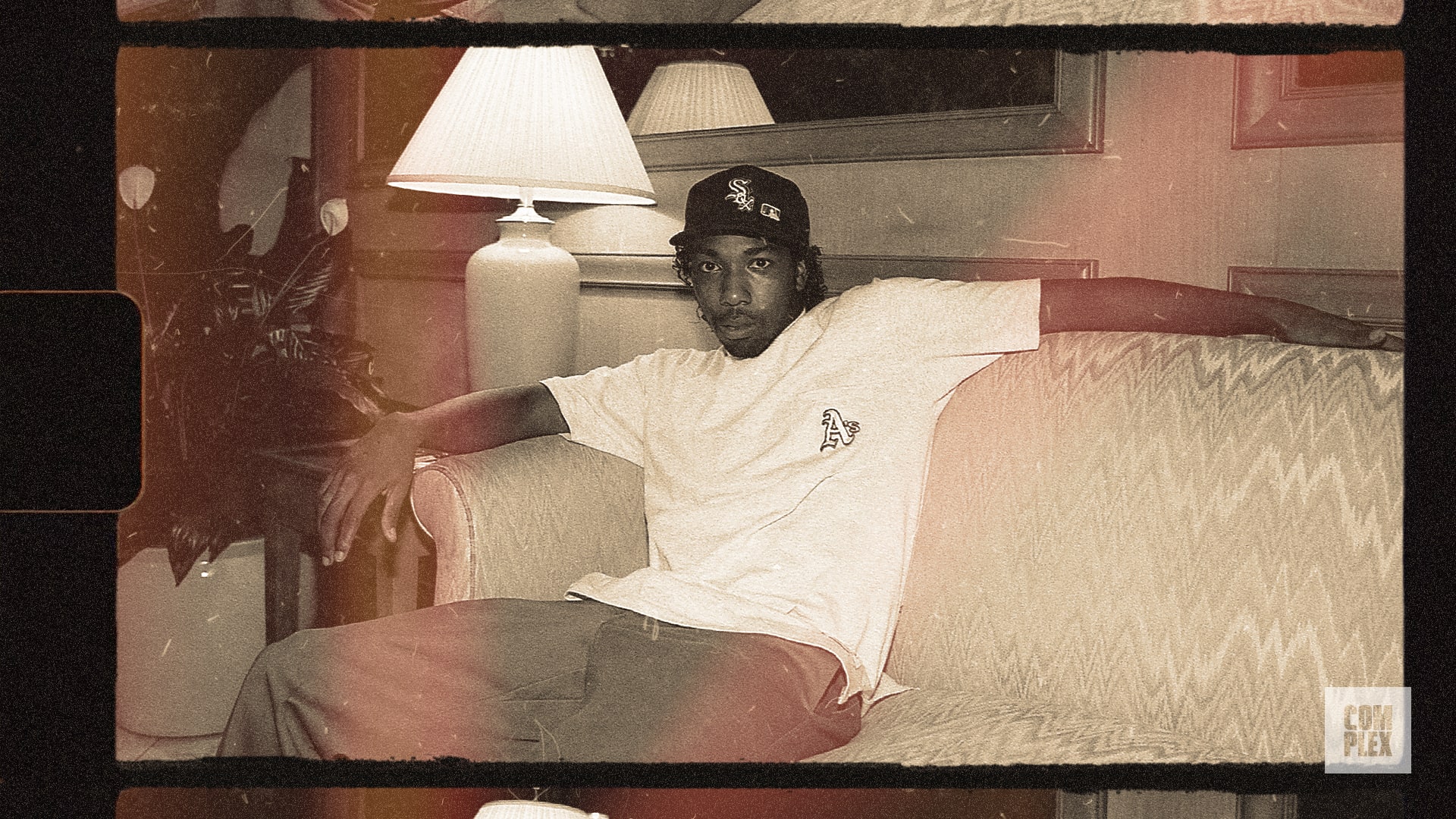 A person in a white shirt and cap sits casually on a sofa in a vintage-style photo.