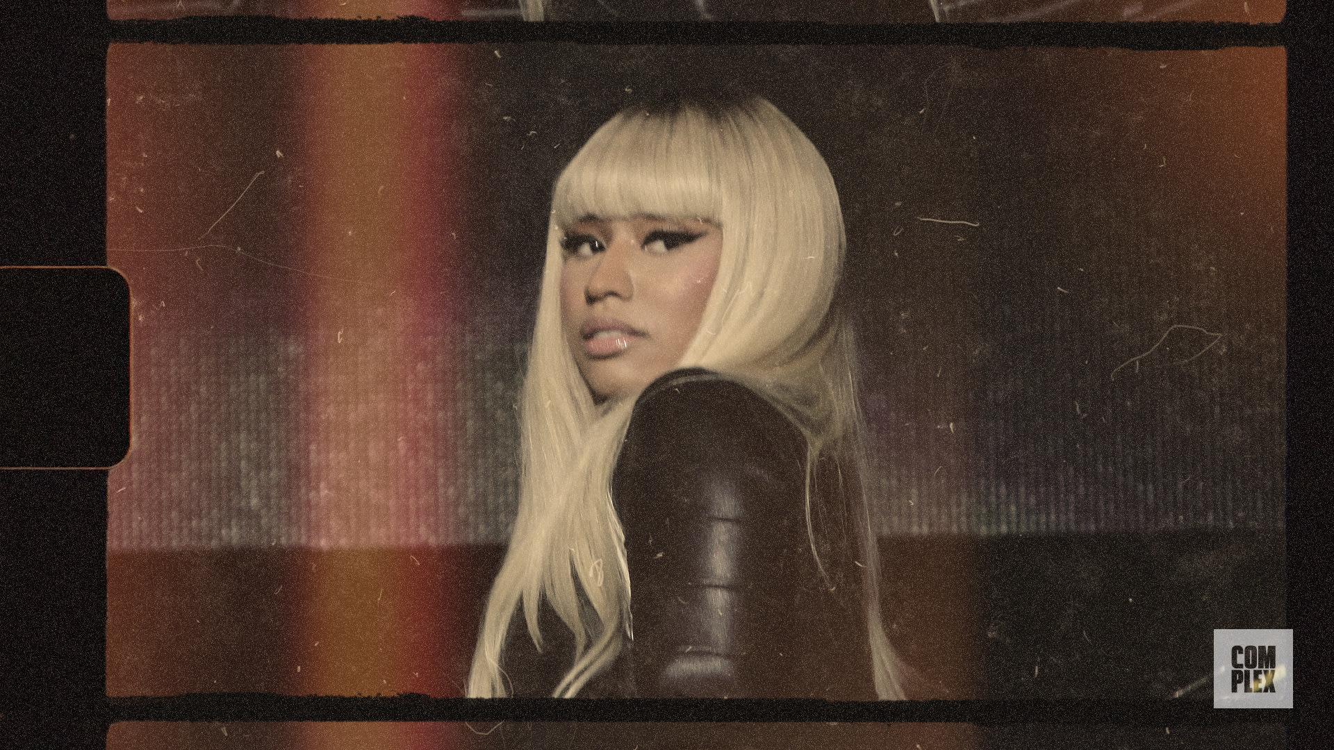 Nicki Minaj with long blonde hair and a black outfit, looking over her shoulder. Retro film effect.