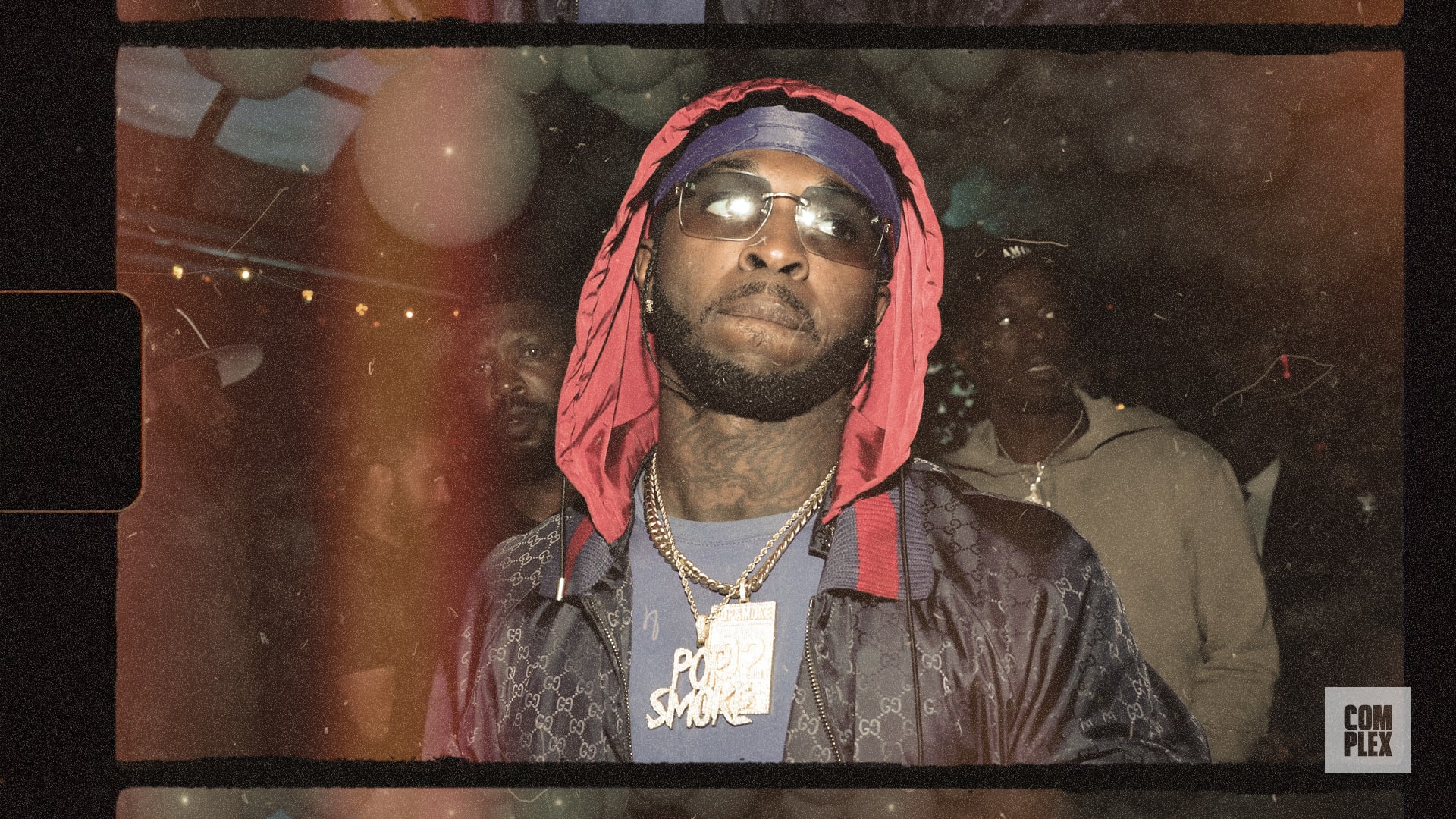 A man wearing a red hooded jacket, sunglasses, and a 