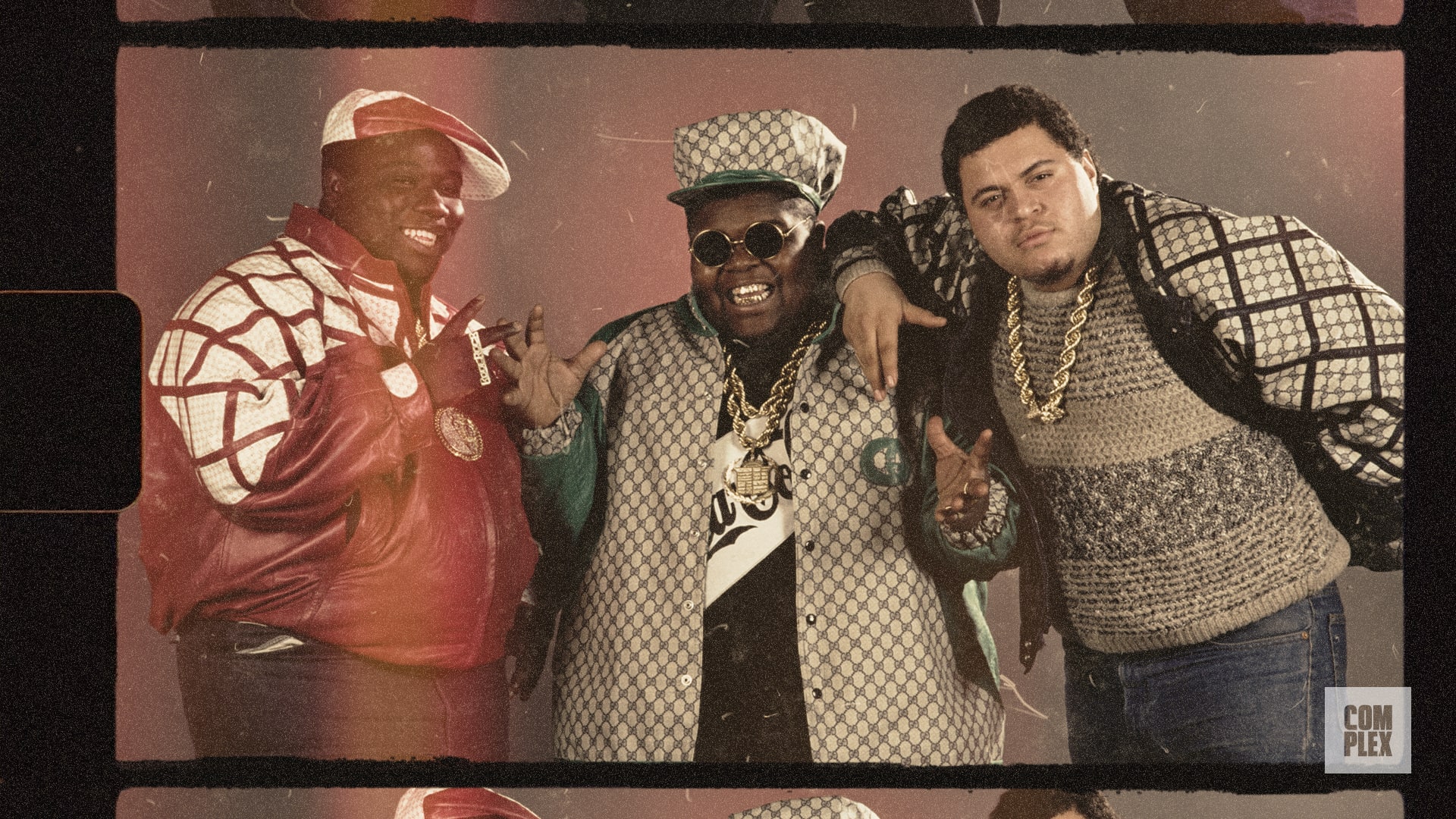 Three men in vintage hip-hop attire, wearing oversized jackets, hats, and gold chains, posing together against a retro backdrop.