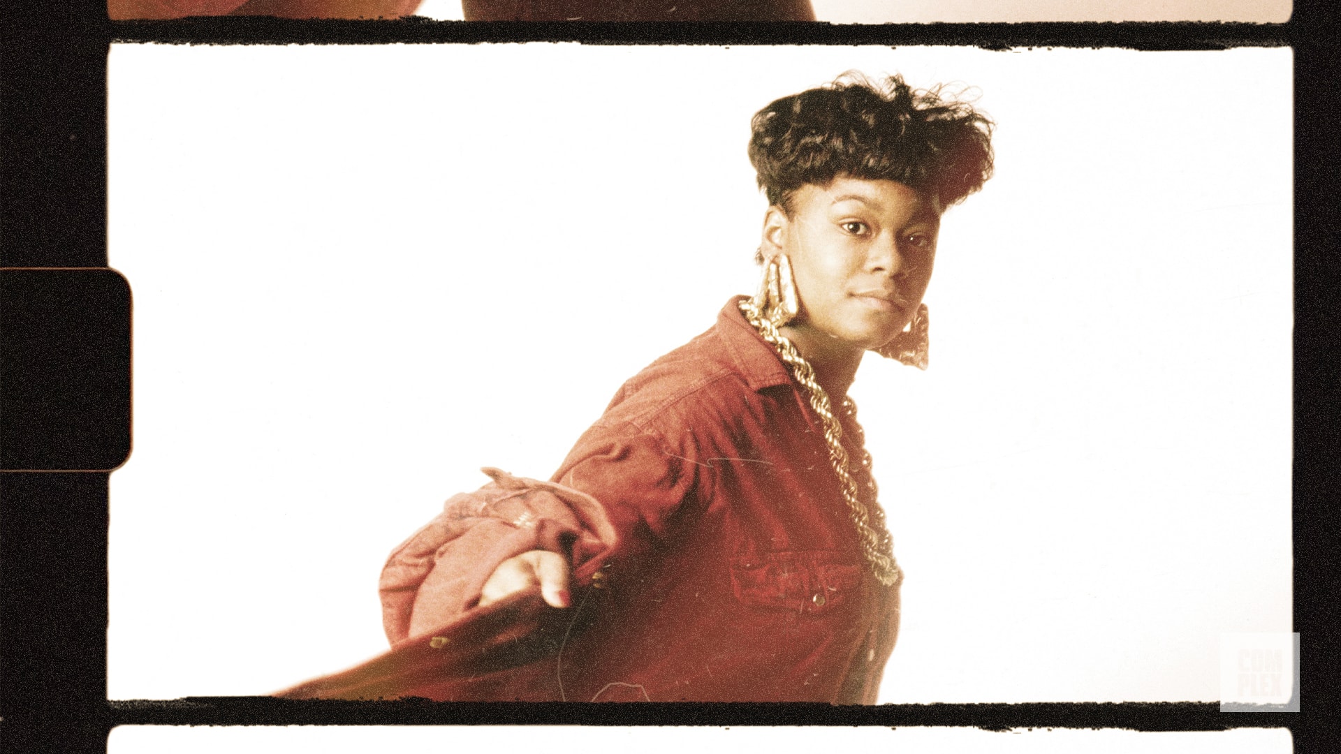 A woman in a red jacket and large gold earrings poses confidently against a white background.