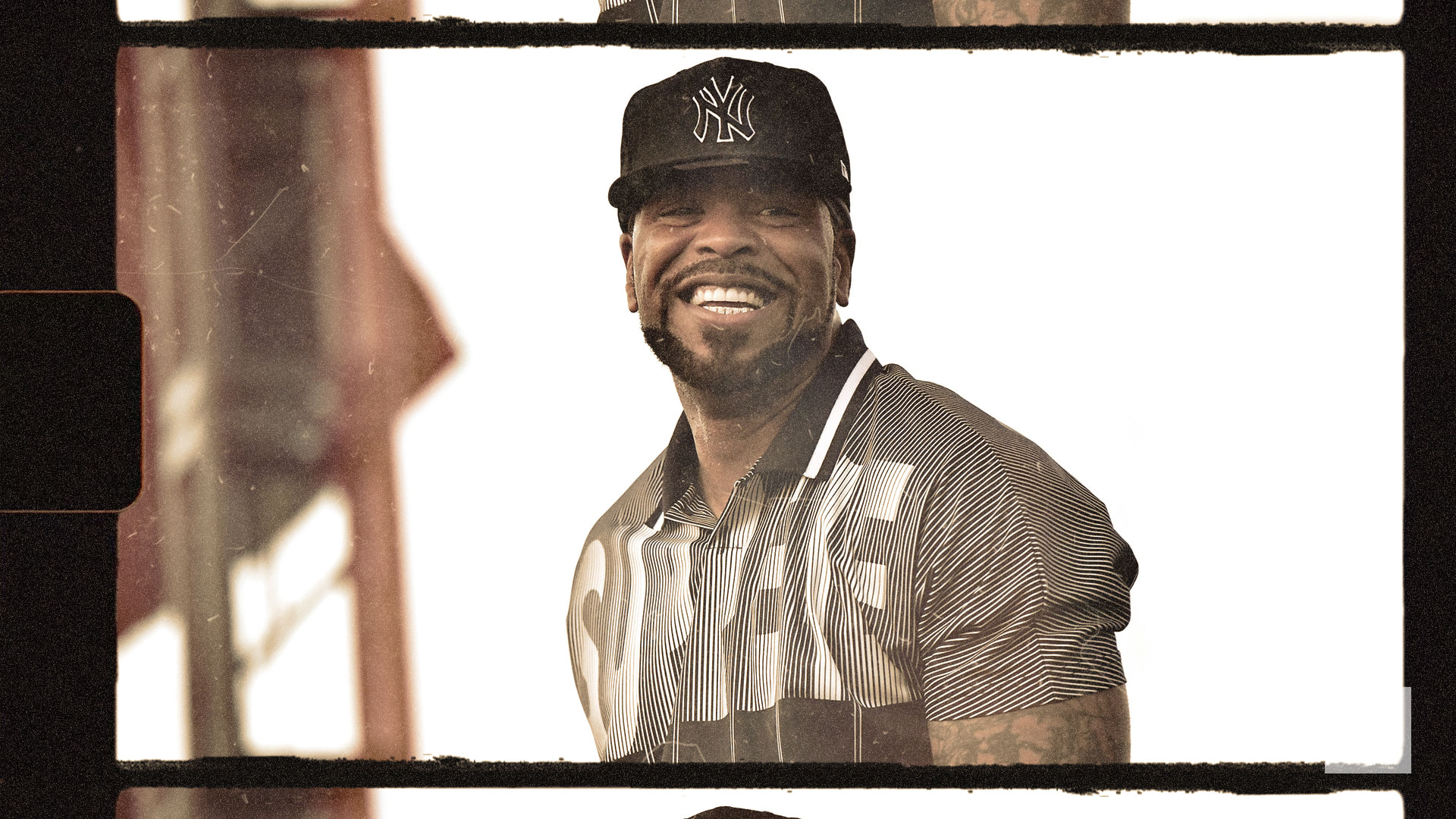A man wearing a New York Yankees cap and a striped shirt smiles broadly. The image has a vintage film effect.