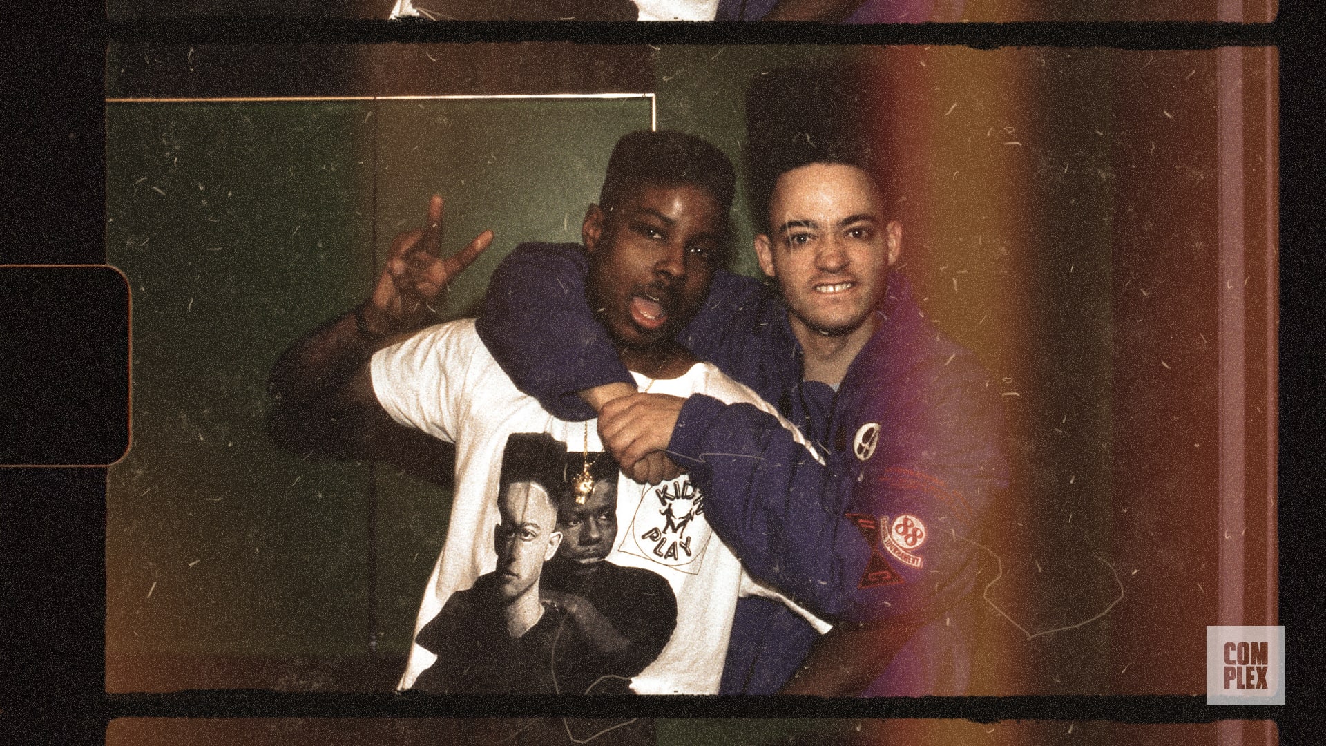 Two men posing together; one wears a graphic t-shirt, the other a blue jacket. The photo has a vintage film effect.