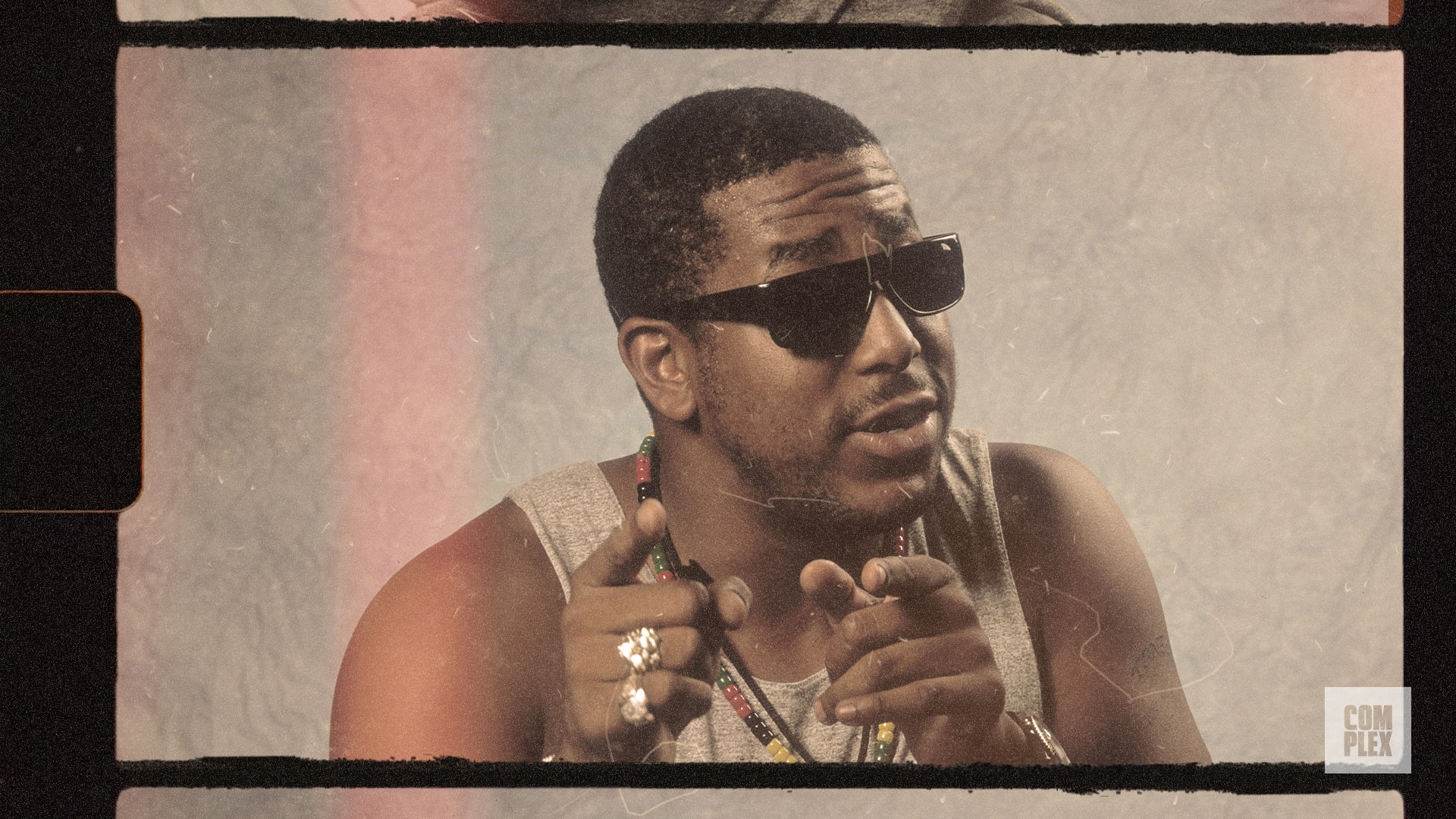 A man wearing sunglasses and a sleeveless shirt, pointing with both hands, with a vintage photo effect.