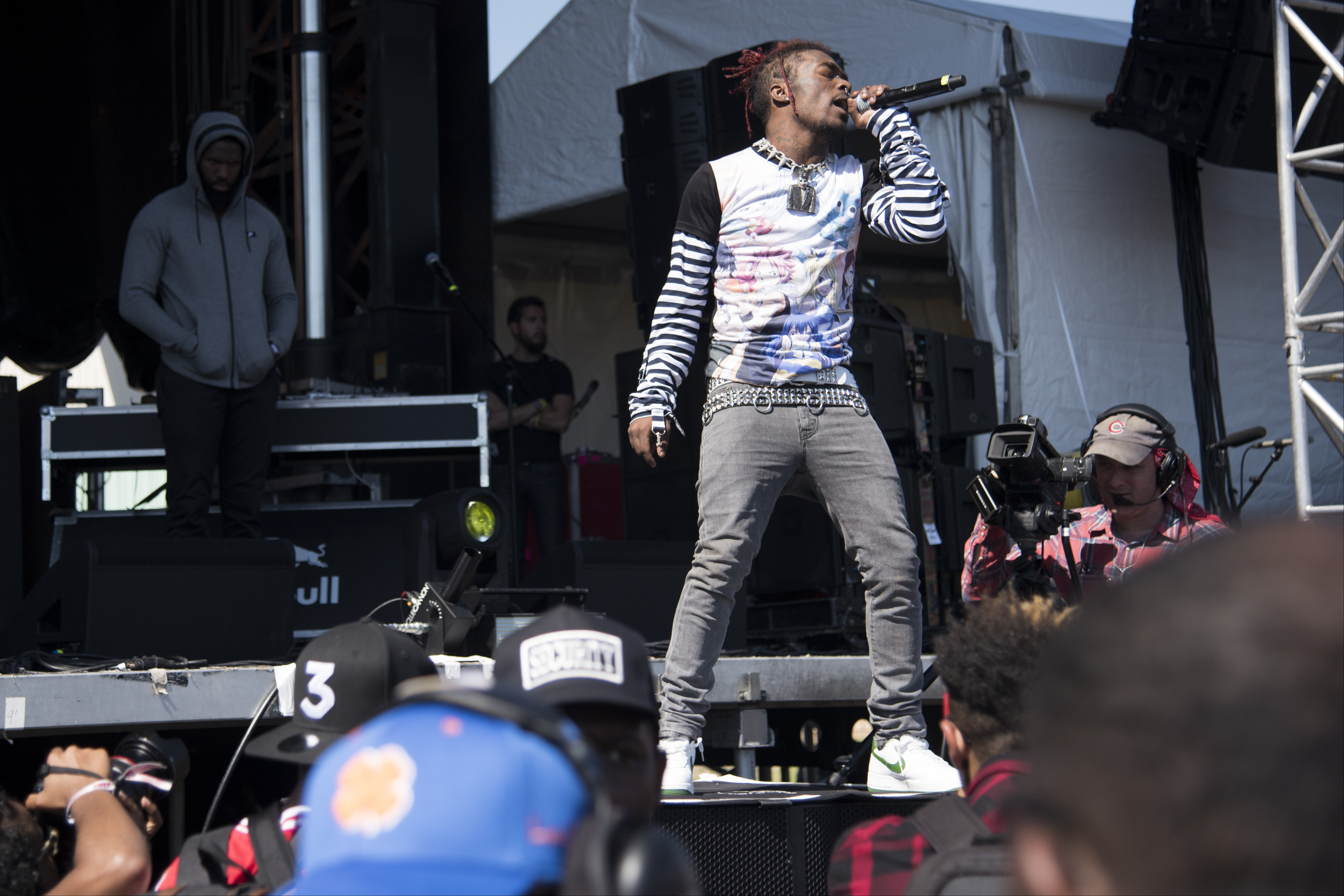 Lil Uzi Vert on stage singing into a microphone. The crowd is watching, and a cameraman is filming the event.
