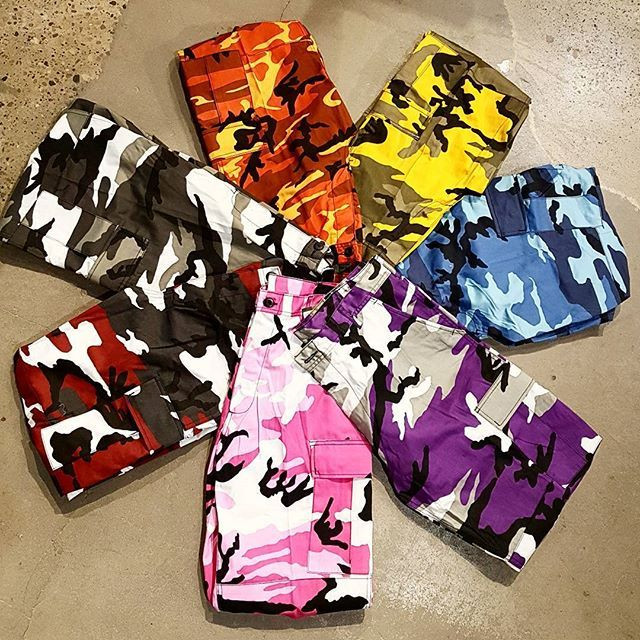 Colorful camo cargo shorts arranged in a circle on a concrete floor.