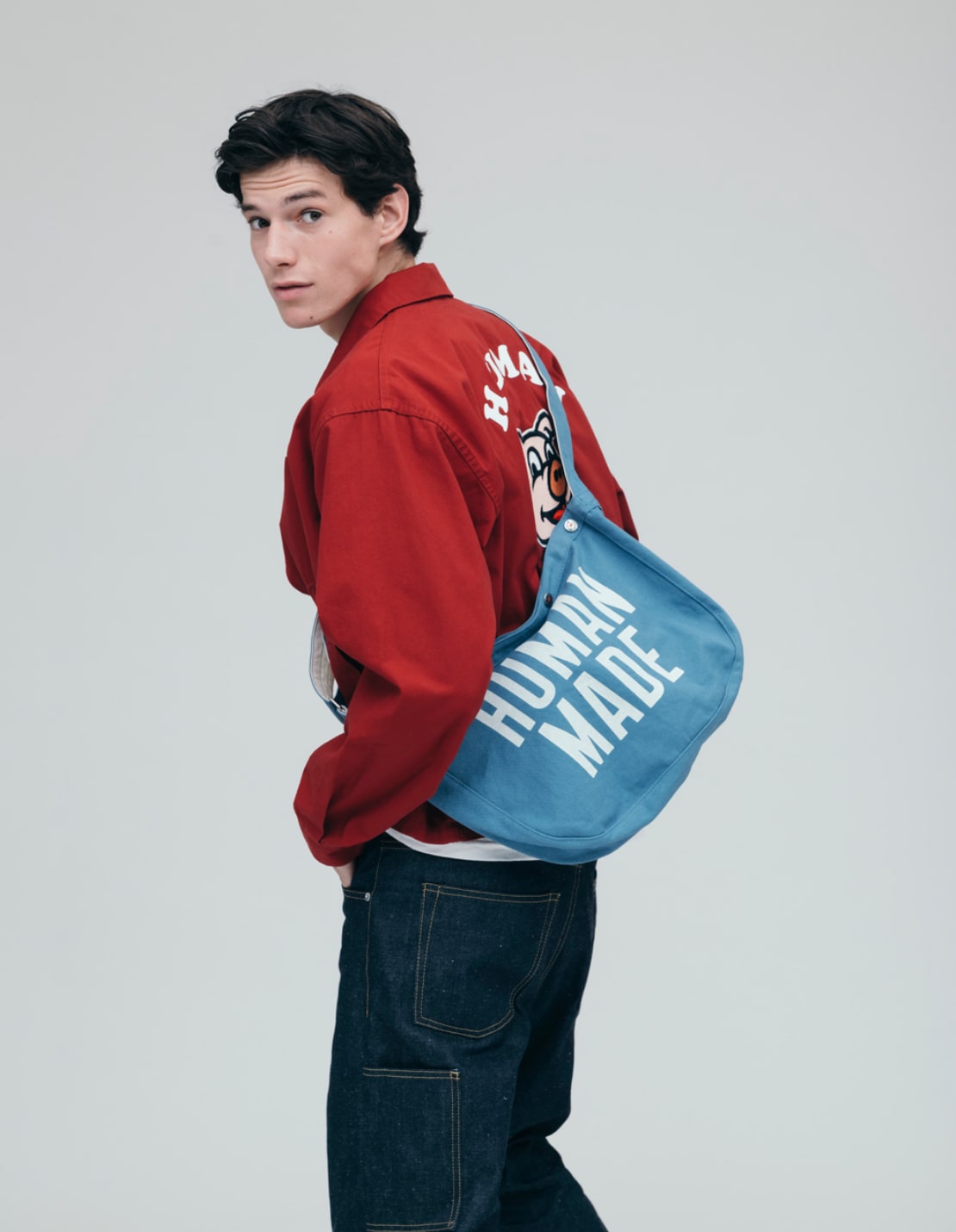 A man wears a red jacket with a blue sling bag, both labeled 